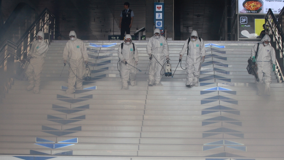 Workers wearing protective gears fumigate and spray antiseptic solution as a precaution against the spr