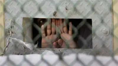 In this 2006 photo, a detainee peers out through the so-called 'bean hole', which is used to pass food and other items into cells [Brennan Linsley/AP]