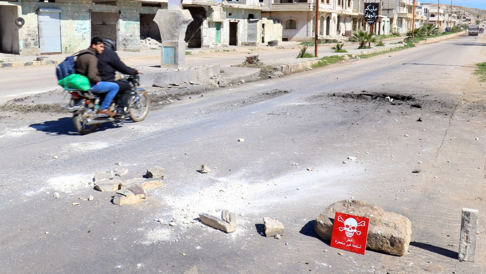 Men ride a motorbike past a hazard sign at a site hit by an airstrike on Tuesday in the town of Khan Sheikhoun in rebel-held Idlib