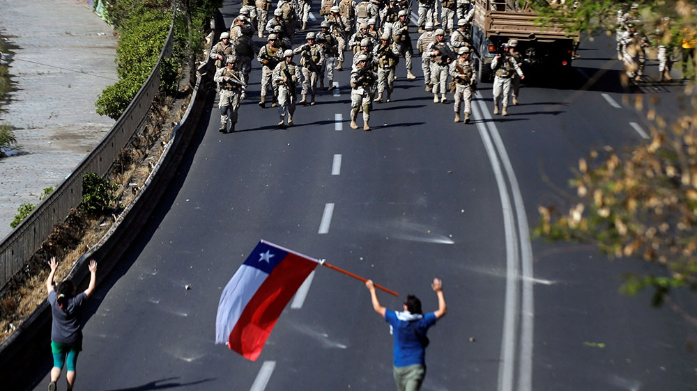 Chilean soldiers gather near demonstrators, one of whom holds a Chilean flag, during a protest