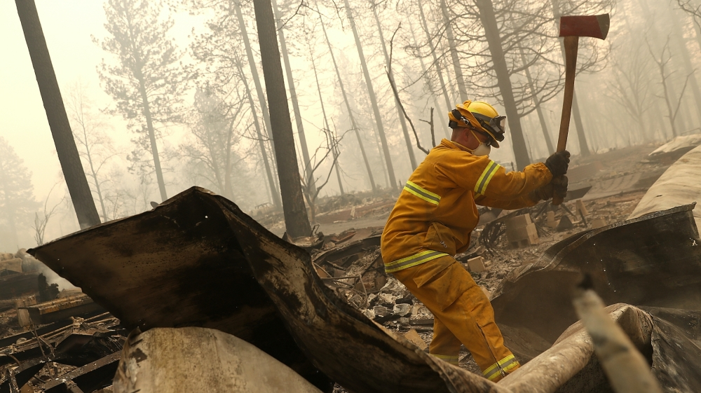 A San Francisco firefighter uses an axe to dismantle a burned mobile home as he searches for human remains at a mobile home park that was destroyed by the Camp Fire on November 14, 2018 in Paradise, California