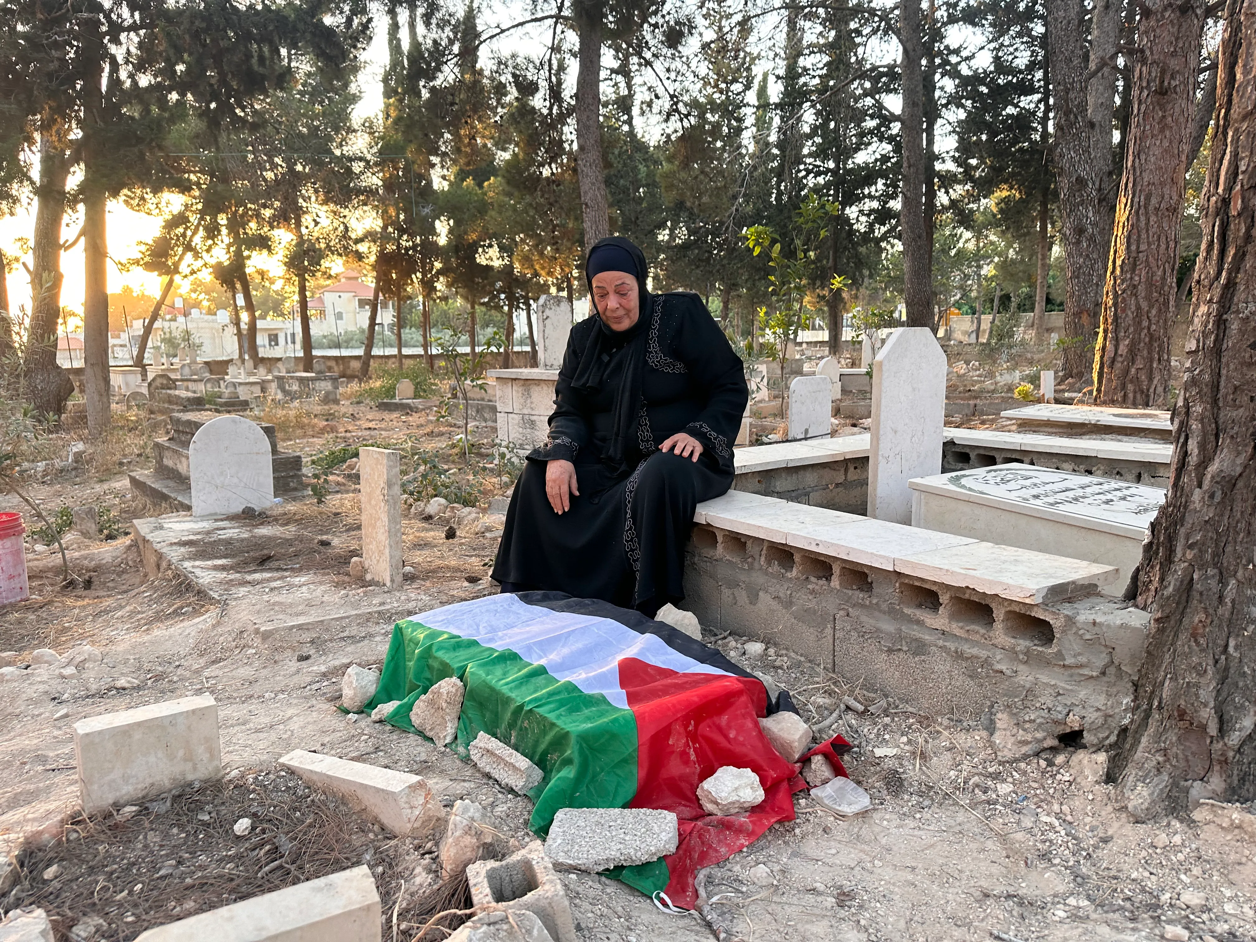 A woman sits beside a grave draped in a Palestinian flag.